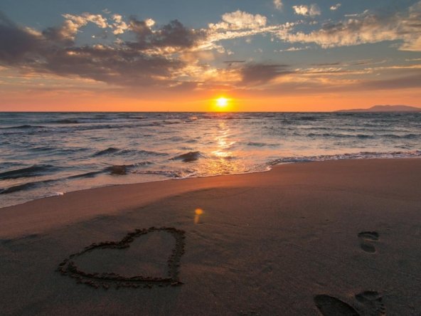 Beautiful sunset over ocean with a heart shape in the sand, perfect for romantic themes.
